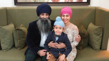 Karen sitting on a green sofa with her husband and their son on her lap - all three dressed up in suits, a dress and turbans.