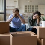 Exhausted couple sit near cardboard boxes at relocation day