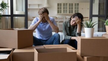 Exhausted couple sit near cardboard boxes at relocation day