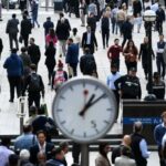 A busy scene at Canary Wharf in London, showing a large crowd of workers walking through the area.