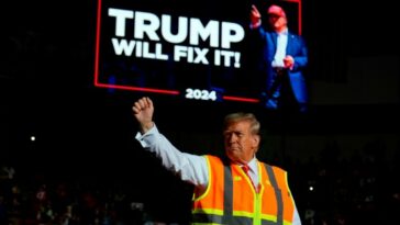 Donald Trump gestures in front of a political display board that reads ‘Trump will fix it!’