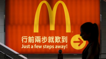 A silhouette of a person in China walking past an illuminated McDonald’s sign.