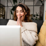 Excited woman looking at laptop screen sitting on cozy sofa at home