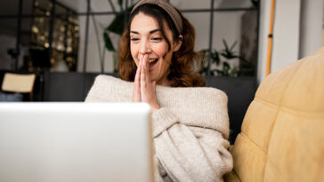 Excited woman looking at laptop screen sitting on cozy sofa at home