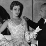 Christian Dior (1905 - 1957) French couturier, with a mannequin in one of his own designs, a satin evening gown called Blenheim.