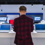 Customer browsing laptops in a store, reflecting 2024 PC shipment growth driven by hardware refresh cycles and Windows 10 end-of-support.