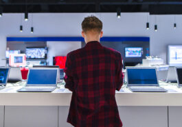 Customer browsing laptops in a store, reflecting 2024 PC shipment growth driven by hardware refresh cycles and Windows 10 end-of-support.