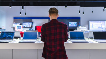 Customer browsing laptops in a store, reflecting 2024 PC shipment growth driven by hardware refresh cycles and Windows 10 end-of-support.