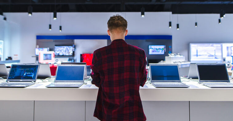 Customer browsing laptops in a store, reflecting 2024 PC shipment growth driven by hardware refresh cycles and Windows 10 end-of-support.