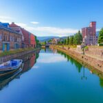 A scenic view of Otaru canal in Otaru, Japan, with houses on either side and a boat sat on the water.