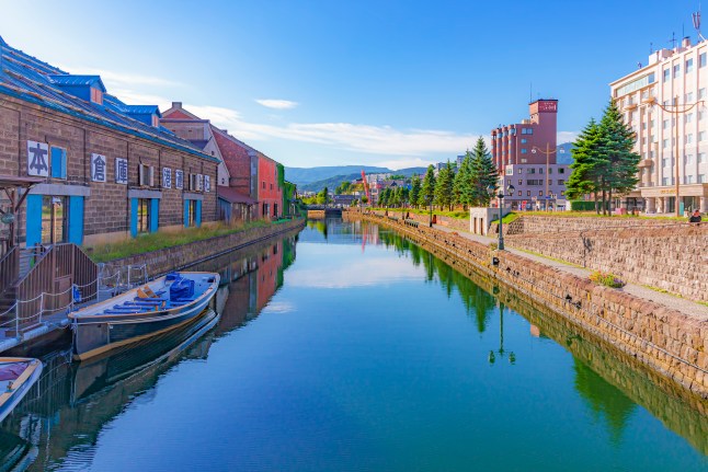 A scenic view of Otaru canal in Otaru, Japan, with houses on either side and a boat sat on the water.